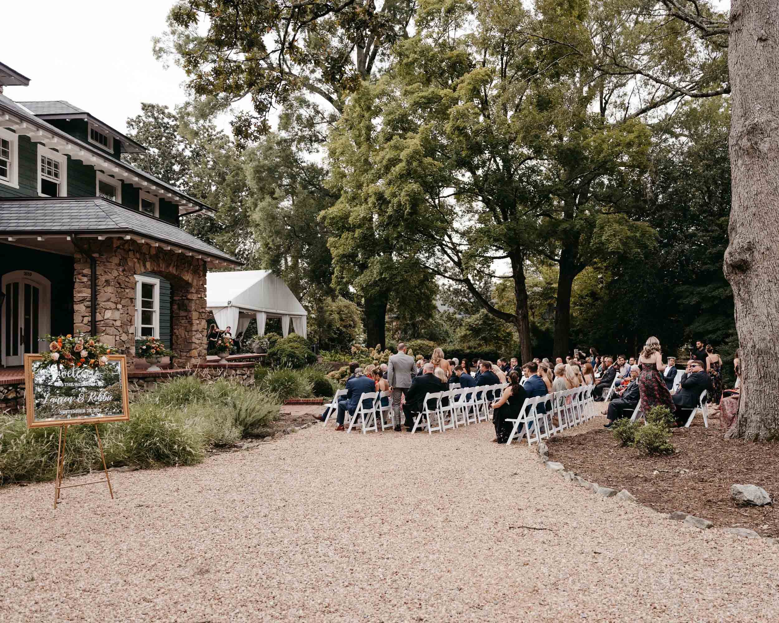 A wedding ceremony taking place at an inn, featuring a couple exchanging vows surrounded by guests and floral decorations.